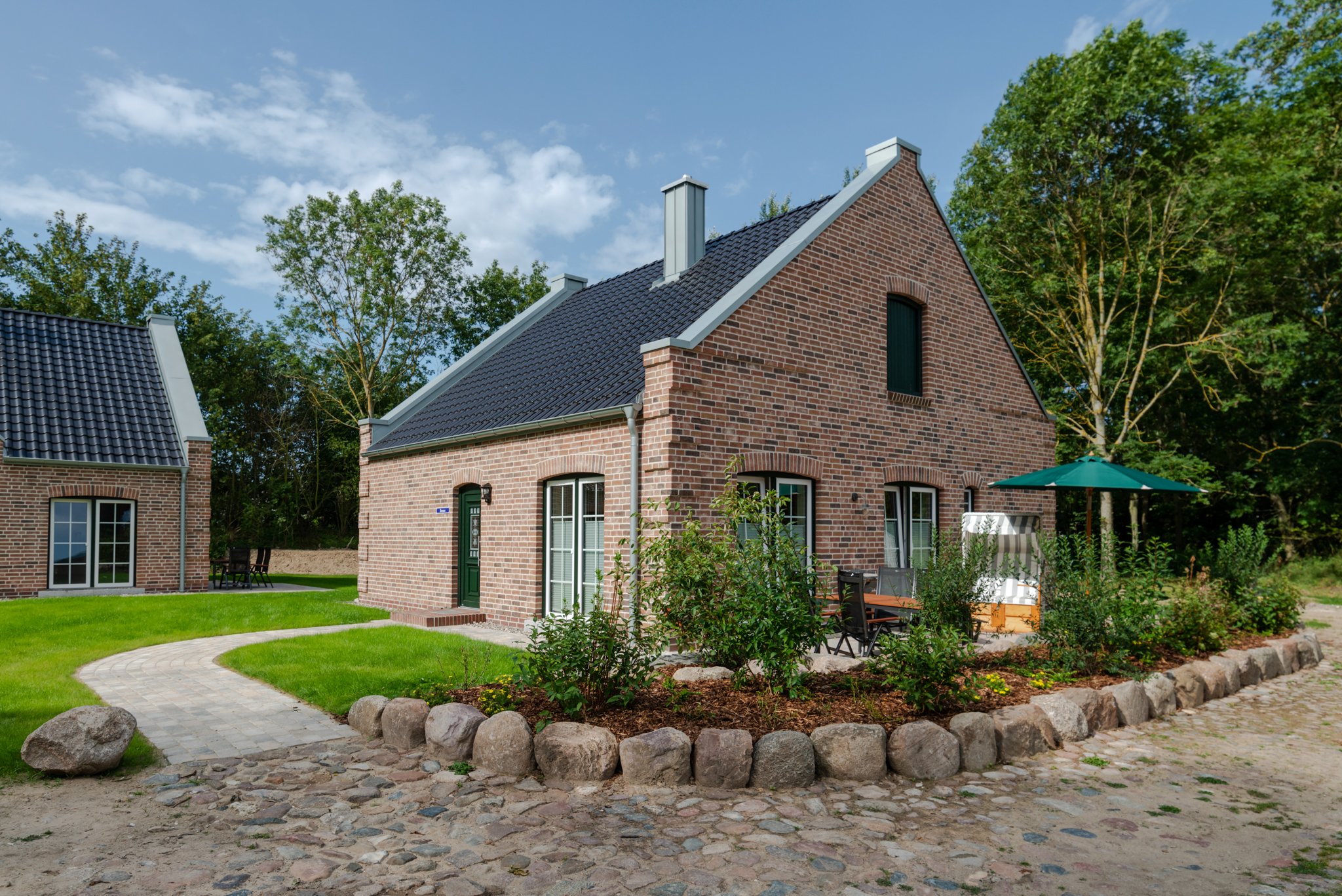 Rotes Backsteinhaus auf Fehmarn mit Terrasse, Gartenstühlen und einem Strandkorb im Garten.