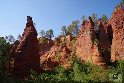 Paysage d'ocre du Roussillon, avec des falaises aux teintes jaunes, oranges et rouges sous un ciel bleu clair