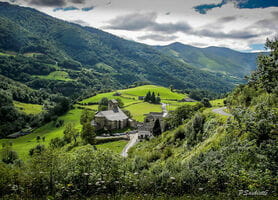 Vue panoramique sur les montagnes du Pays Basque en été, avec le petit village de St Engrâce et son église en arrière-plan, offrant une perspective impressionnante sur les paysages verdoyants et escarpés de la région.