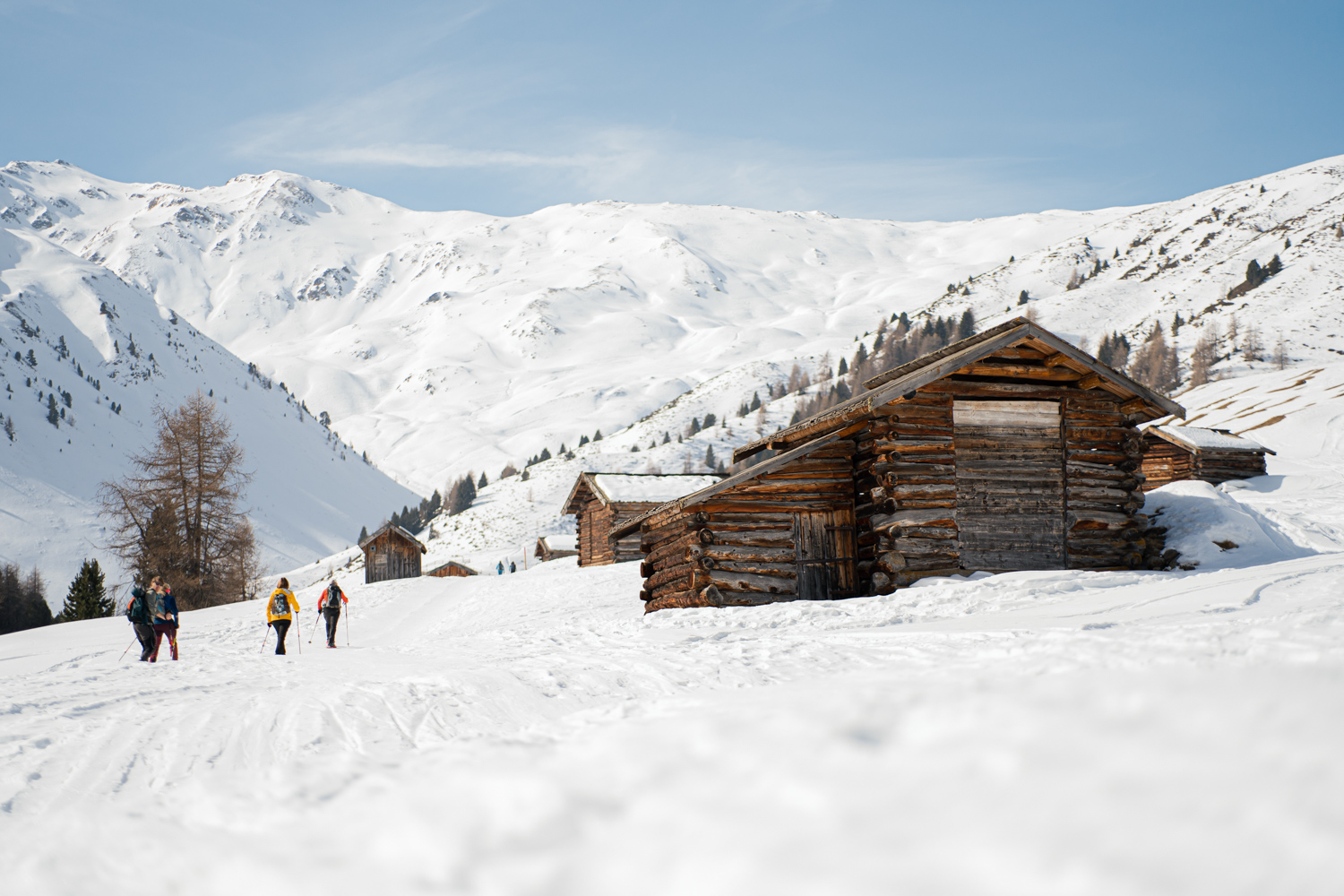 A snow-covered mountain landscape with wooden huts and hikers in the snow.