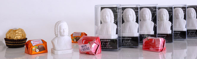 In an extremely wide format, six eraser busts are lined up staggered in transparent boxes in the right half. On the left is an unpacked bust. There are 2 Mon Cheri, 1 Ferrero Küsschen and 1 Rocher for decoration and scale.