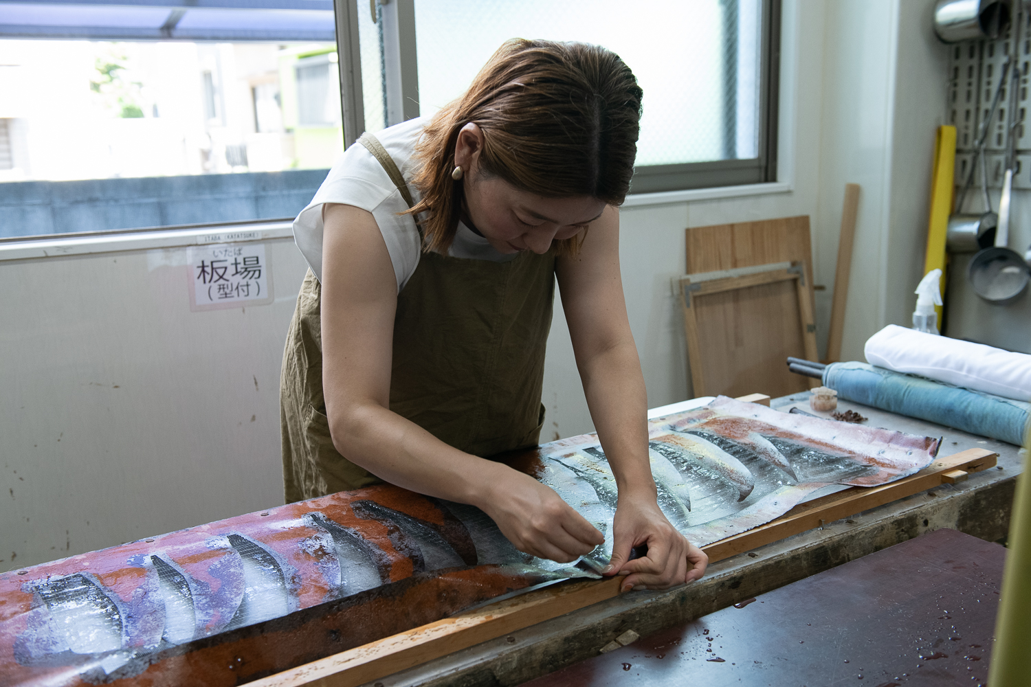 ▲「板場（いたば）」での作業。型紙（柿渋紙にオリジナルデザインの模様を掘ったもの）を枠型に打ち付ける。