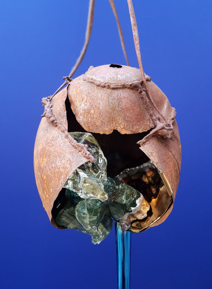 haengendes, explodiertes Stahlei in dem Glas zu sehene ist und aus dem blauer Edelstahl trieft, www.wuensch-art.de