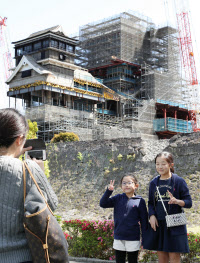 修復作業中の熊本城を背に記念写真に納まる観光客