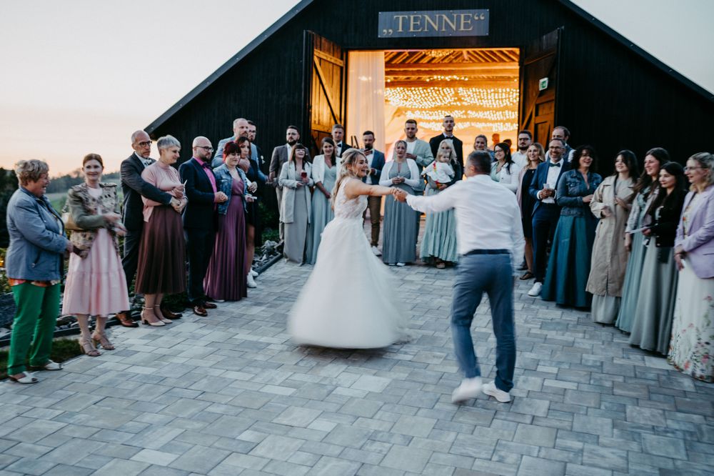 Das Paar wirbelt beim Hochzeitstanz über den Vorplatz der Tenne, im Hintergrund glitzern Lichterketten die aus der Scheuen leuchten.