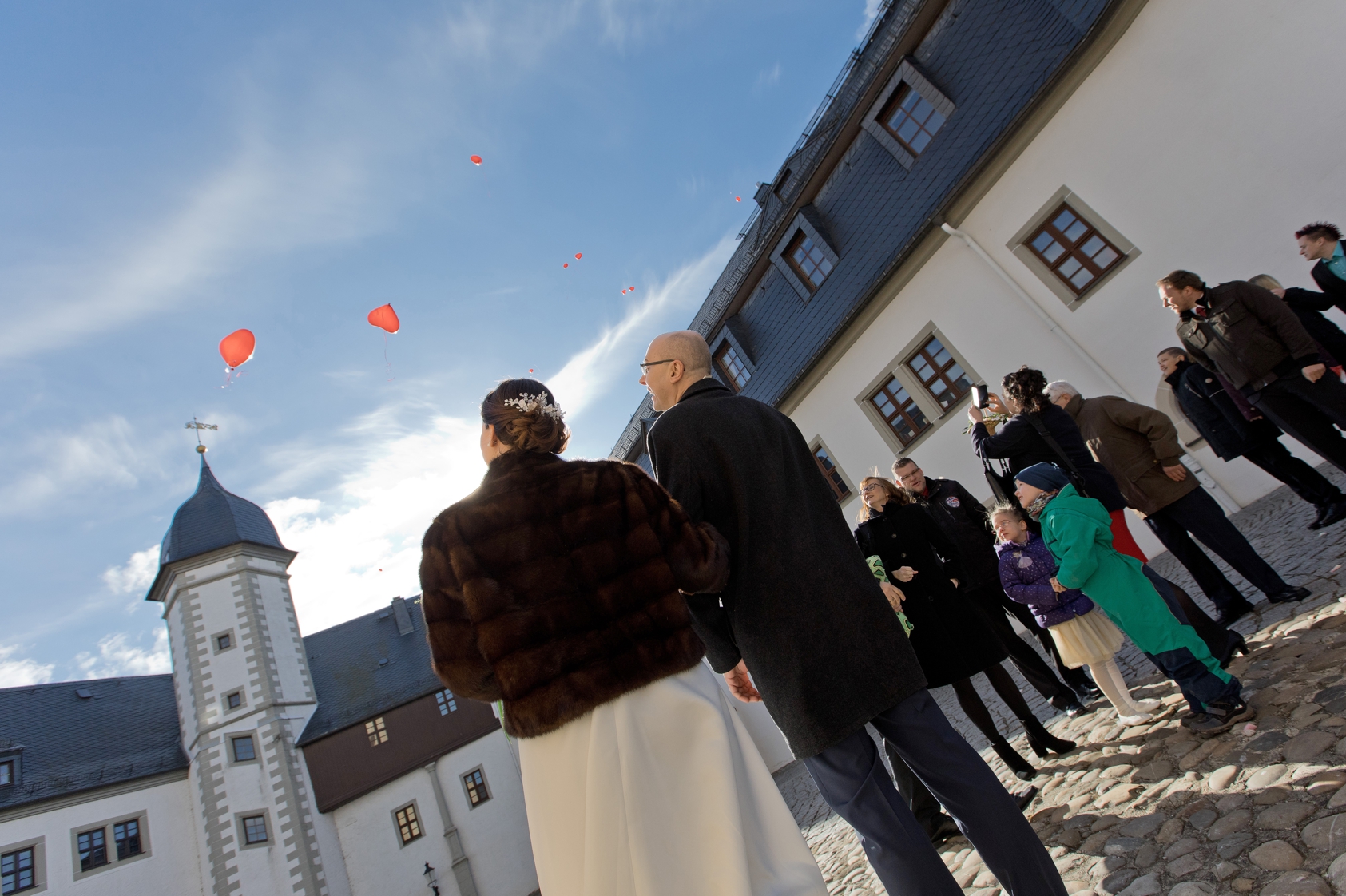 Brautpaar im Schlosshof von Schloss Wildeck in Zschopau lässt Luftballons in den Himmel steigen.