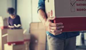 Two people in a house in the process of moving with one person carrying a box