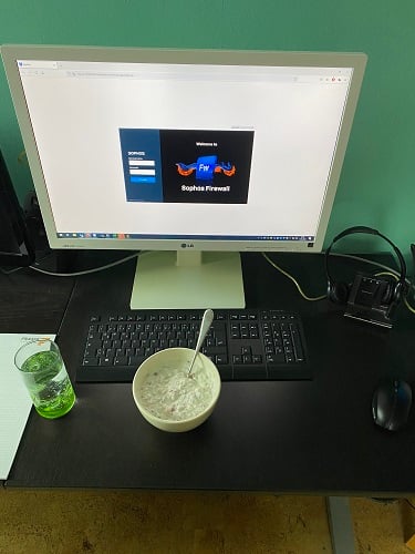 Foto eines Schreibtisch mit Monitor und Tastatur, davor eine Müslischüssel und ein Glas mit einem grünem Getränk