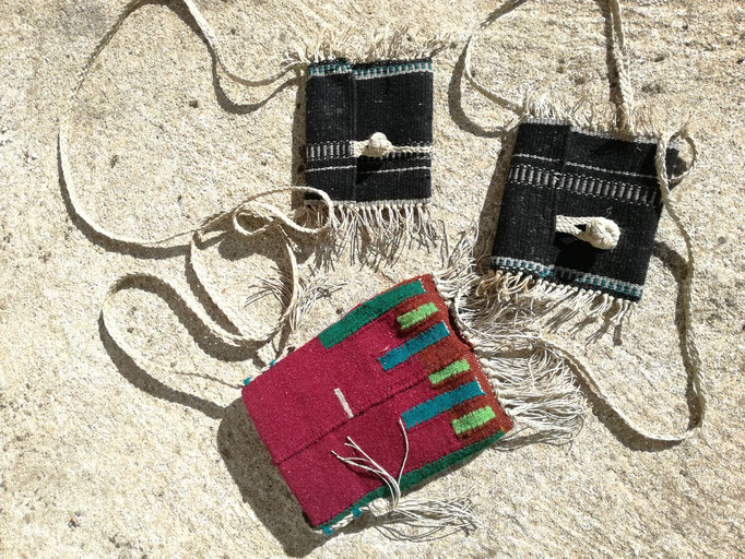 Trois petits sacs-pochettes tissés en laine, un couleur bordeaux avec éléments verts, deux autres noirs avec les motifs gris.