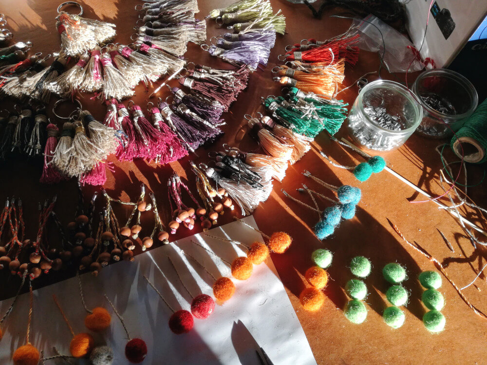 Plan de travail couvert des fils de la laine de toute couleur mélangés, des balles en laine feutrée et des porte-clés déjà finis avec petites pelotes de feutre. 