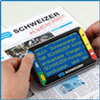 Zwei Hände halten eine elektronische Lupe über einer Zeitung