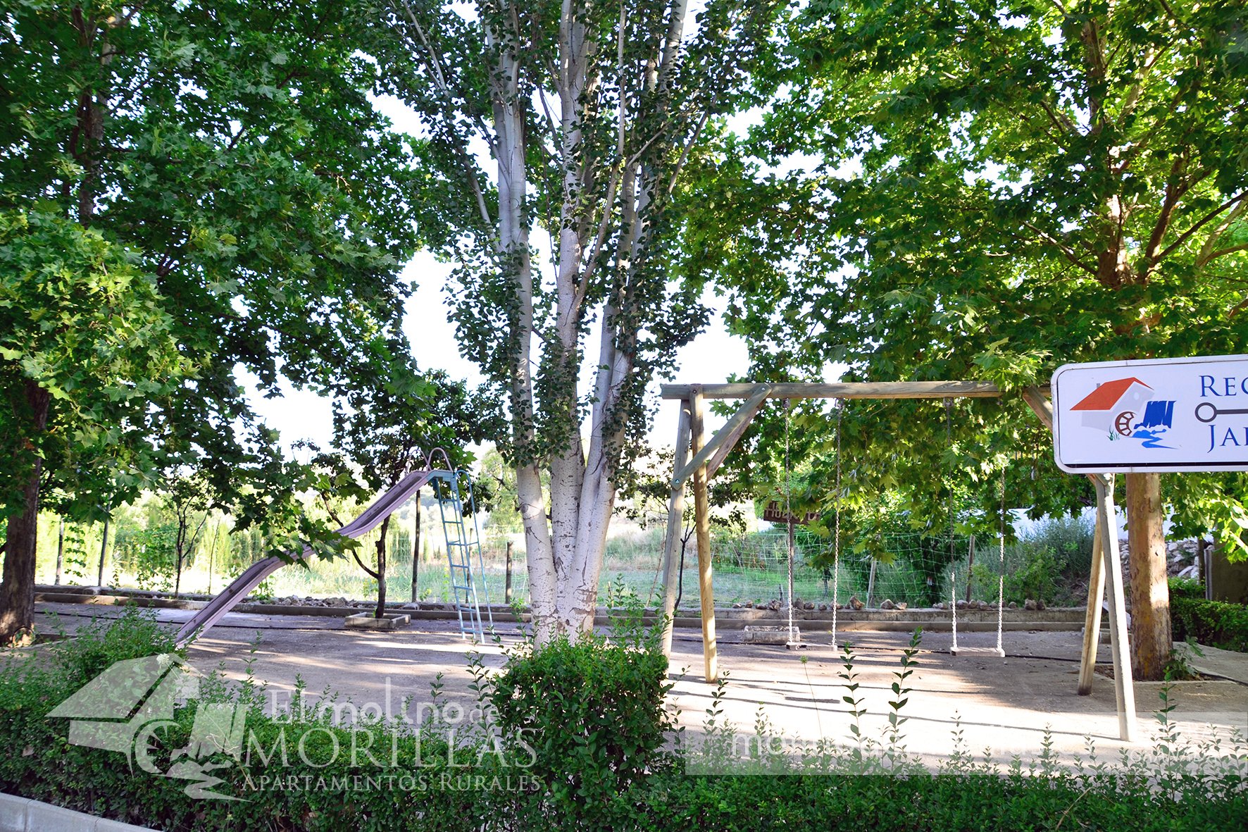 Parque infantil entre álamos y frutales
