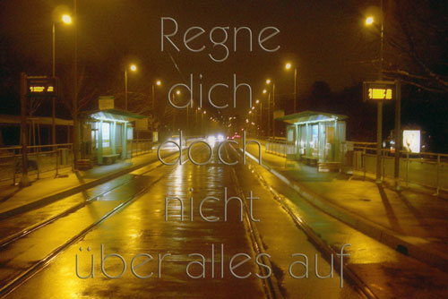 nächtliche Tramhaltestelle im Regen, darüber in grossen Lettern: Regne dich doch nicht über alles auf.