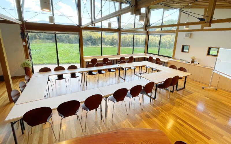 【ご利用イメージ３】木製テーブルと折畳み長テーブルを使って、比較的人数の多い会議をすることもできます。円卓に着席できるのは２３名程度ですが、ケヤキのテーブルやカウンター席を使用したり、着席のみの席をつくることも可能です。