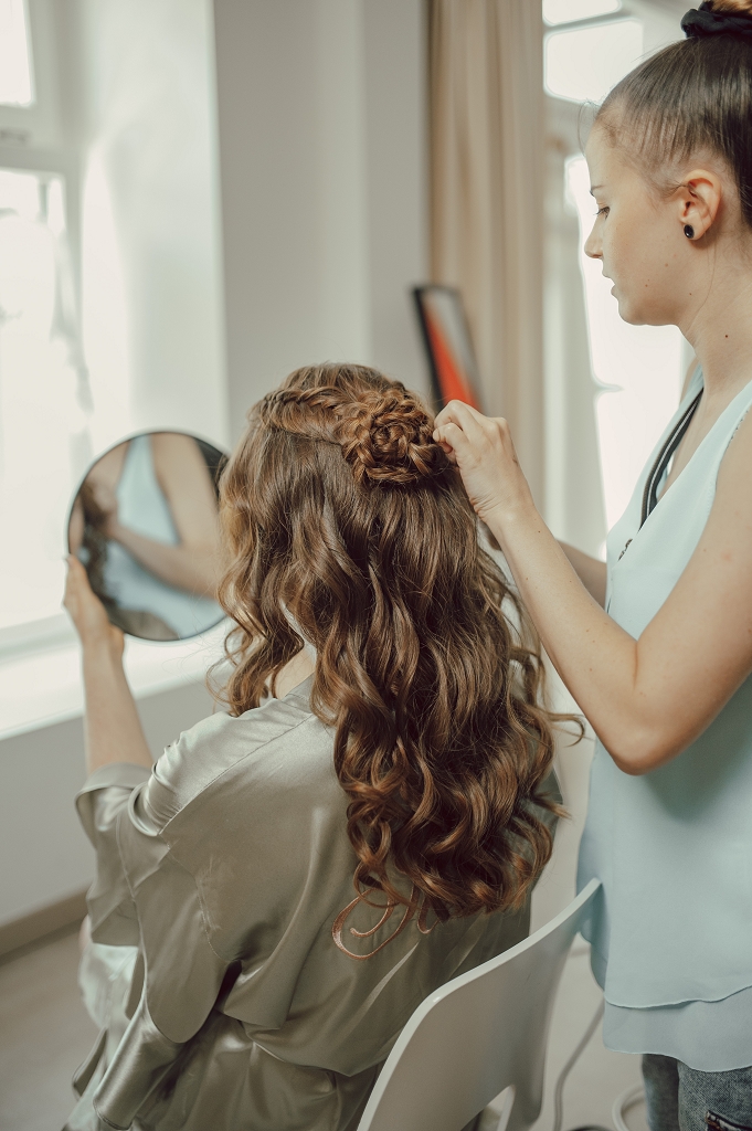 Haarstylistin bei der Arbeit frisiert Braut halboffen mit Zopfblume