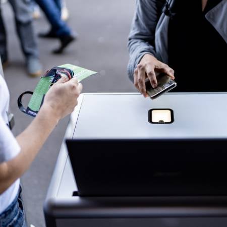 Eine Person hält ein Handy über einen Scanner eines SelfPrint-Kiosks, der Badges einer Veranstaltung druckt.
