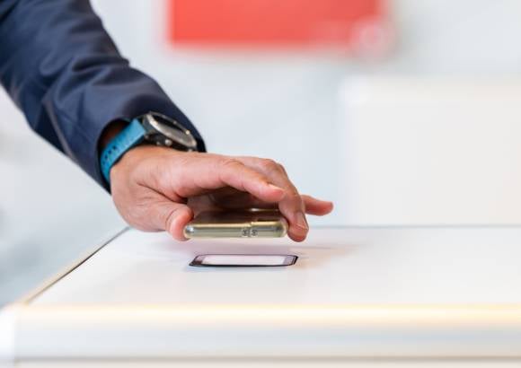 Ein Hand hält ein Smartphone über einen Scanner von einem SelfPrint-Kiosk.