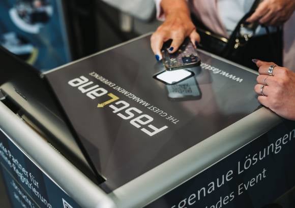 Leicht schräg von oben fotografierte Hand hält eine Hand mit Smartphone über einen Scanner von einem SelfPrint-Kiosk.