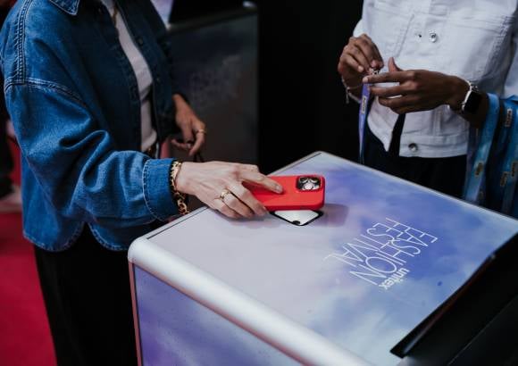 Leicht schräg von oben fotografierte Hand hält eine Hand mit Smartphone über einen Scanner von einem SelfPrint-Kiosk.