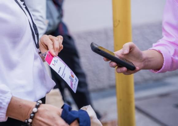 Eine Hand hält einen mobilen Einlassscanner und scannt ein Badge mit QR-Code.