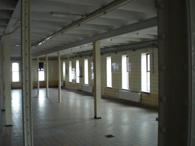 Interieur van het pakhuis: zware, dicht op elkaar geplaatste balken en stalen kolommen met inkepingen voor de rekken. 