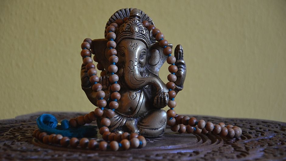 Ganesha Statue auf einem Holztischchen, mit einer Mala umwickelt