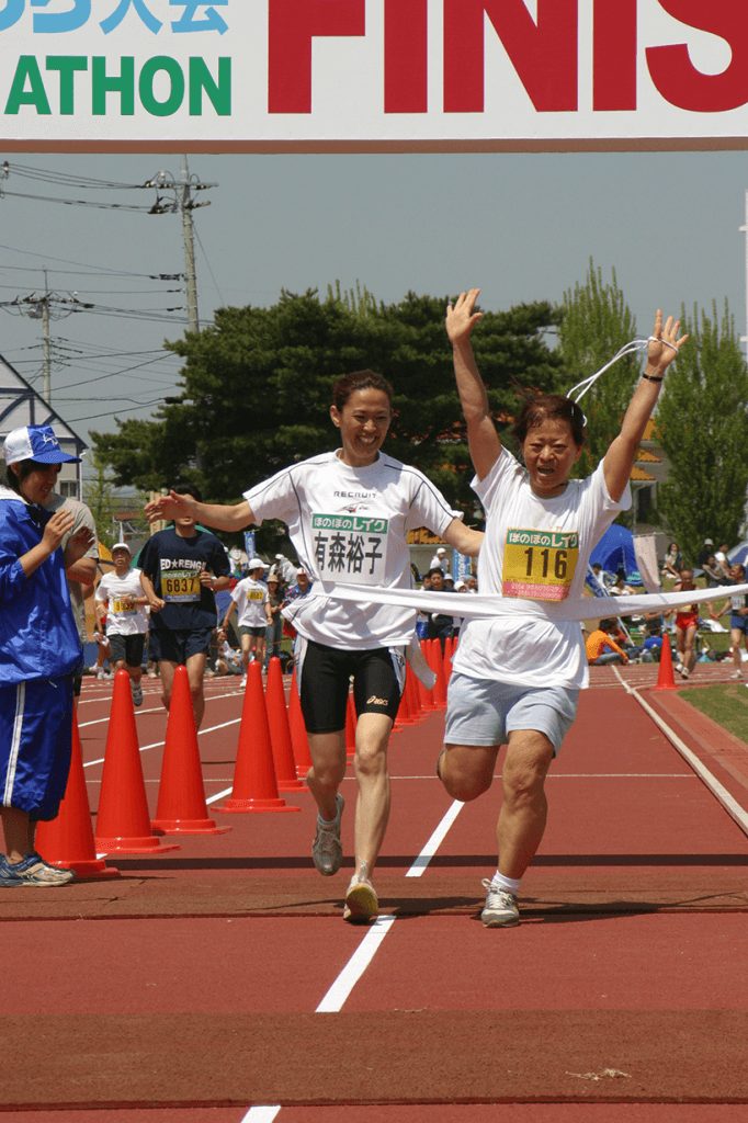 【第14回大会（2004年）】ブラインドランナーとゴールする有森裕子さん。かすみがうらマラソンでは有名ランナーが伴走をして直接ランナーを支えています。