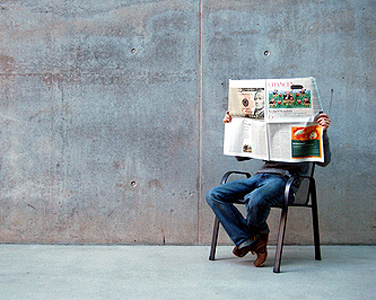 Mann sitzt in einem leeren Raum auf einem Stuhl und liest Zeitung