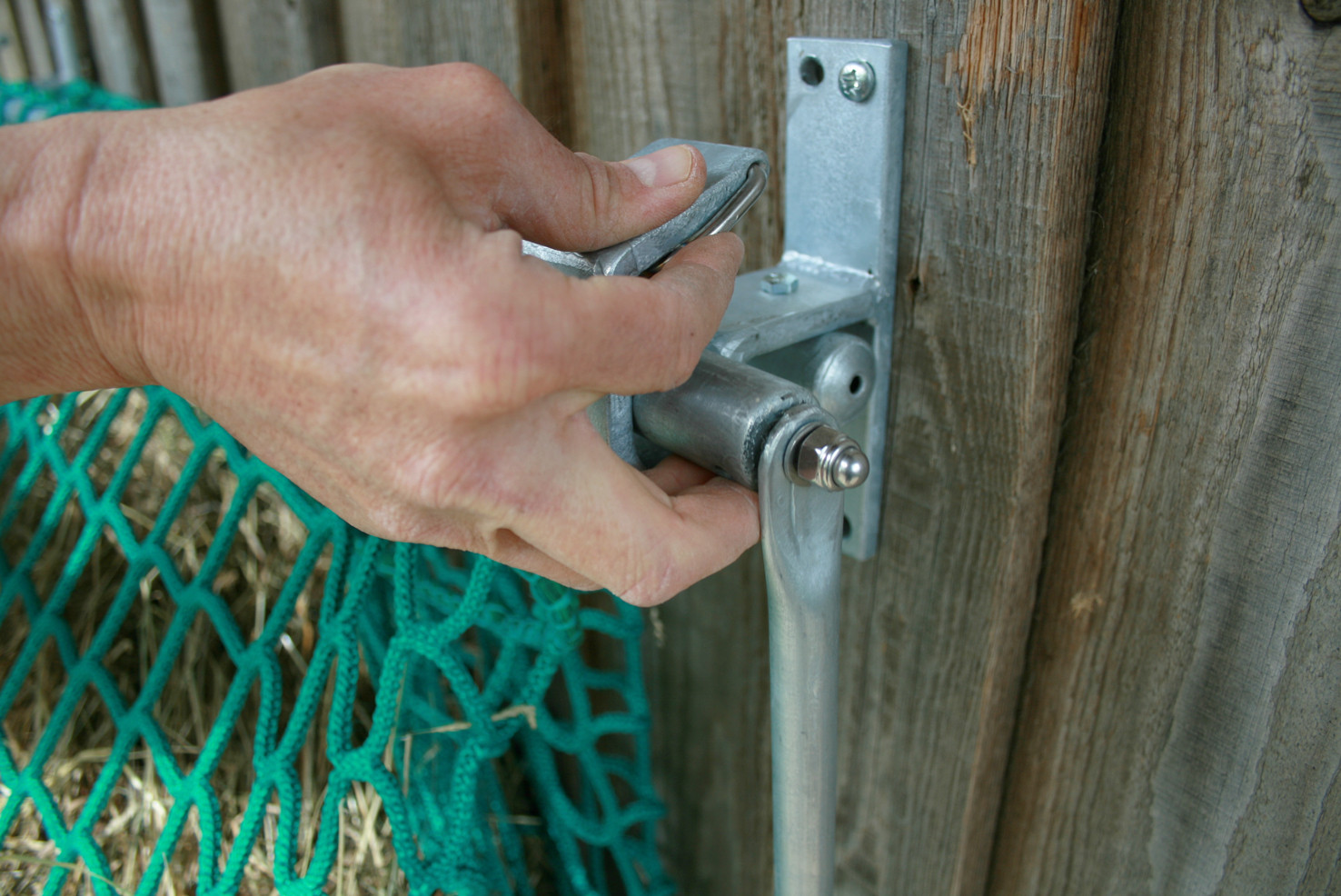 Öffnen der Raufe. Gleichzeitig rechts und links die Verschlussbügel mit den Zeigefingern nach hinten drücken und die vordere Stange herausnehmen.