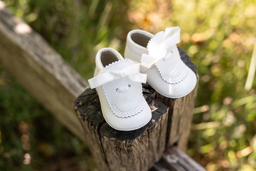 Chaussons baptême bébé fille montants en cuir blanc avec fermeture par un ruban de satin. Magasin vêtements baptême bébé Paris, Neuilly-sur-Seine.