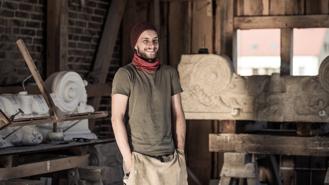 Steinmetz Marcus Scheffczyk steht in Zunftkleidung vor einem Bildhauer-Stück aus Sandstein