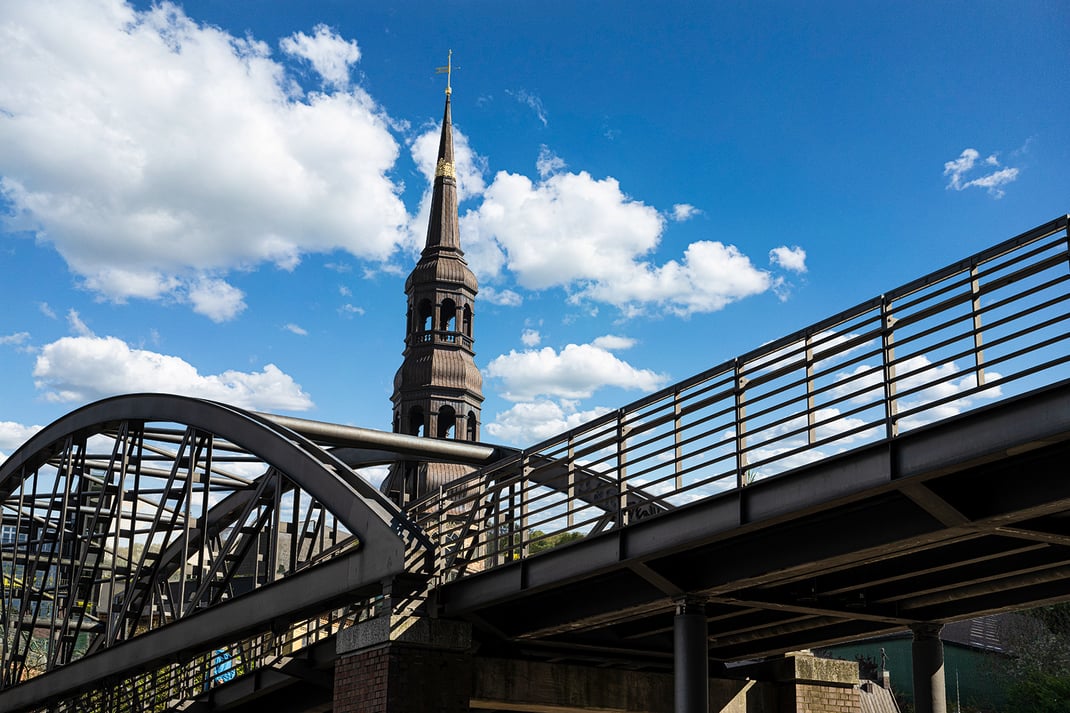 Fotoauf einen Kirchturm über eine Brücke im Vordergrund gegen blauen Wolkenhimmel