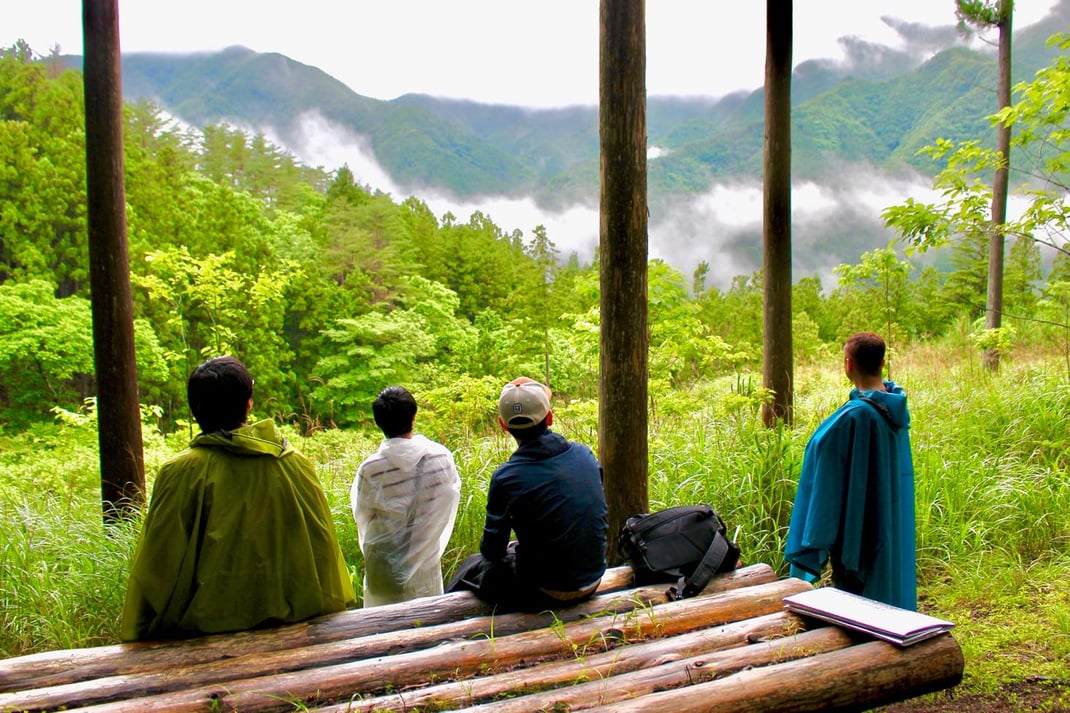 森の中で仲間と一緒に遠くを見つめる瞬間。日常から離れ、言語ではなく非言語で対話を重ねる内省と対話のプログラム-1Day（森の一日）。