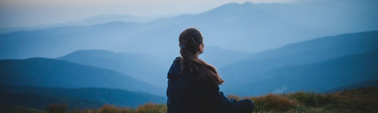 Person sitzt ruhig in weiter Landschaft und blickt in die Ferne, ein Moment von Sammlung und innerer Orientierung in einer Übergangsphase