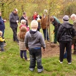 Während H. Lang Rindenmulch auf die Baumscheibe verteilt übergibt Frau Kerner eine Tüte mit Bio-Äpfeln an die Leiterin des Spielhauses Anja Pertler (ganz links)