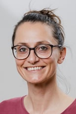 Ein Portrait von Kristin Seifert, Physiotherapeutin in der Praxis Octopus in Graz. Sie trägt eine Brille und hat ein einladendes Lächeln. Sie trägt ein violettes Shirt, der Hintergrund ist wandgrau.