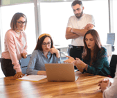 Twee collega's zitten aan een tafel met een latop. Twee collega's staan recht.