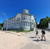 Historic timber bathing pavilion on the beach with two people walking past in in Jurmala, Latvia