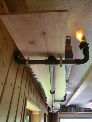 Von der Decke abgehängtes umlaufendes Bücherregal aus stabilem Stahlrohr. Beleuchtung in Form einer Wassrrohrlampe integriert. | (c) S. Erb