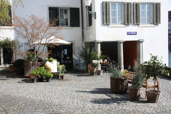 Platz mit Sonnenschirm und Auslage eines Blumengeschäftes. 