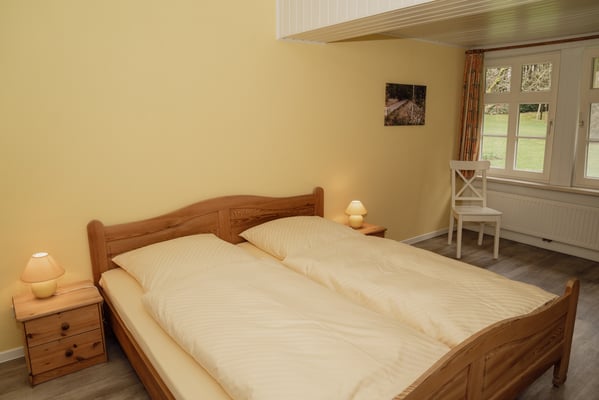 Das Schlafzimmer mit Doppelbett der Wohnung 1 mit warmen Holztönen.