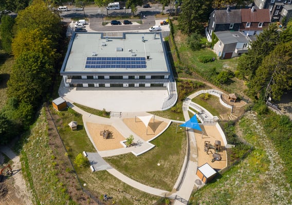 Kita Hatzfelder Straße Wuppertal, Luftaufnahme Ansicht Kindertagesstätte inklusive Blick auf das Dach mit Haustechnik, auf die Kiss & Ride Spur und die Stellplätze