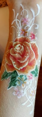 Bodypainting auf dem Unterarm. Eine Rose mit kleinen Blüten und Kringeln drumherum.