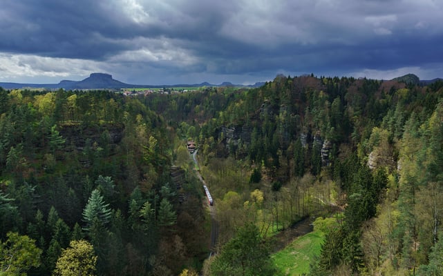 Blick von den Ochelwänden bei Porschdorf hinunter ins Sebnitztal. Auch ein kleines Stückchen Einsicht auf die Strecke bietet sich hier. Dort ist ein Desiro der Nationalparkbahn unterwegs nach Rumburk. April 2017.