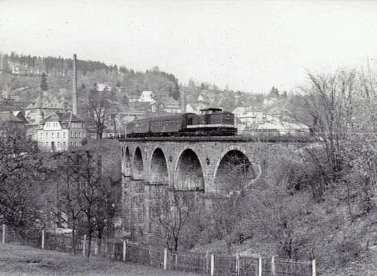 Eine typische Reichsbahngarnitur der 80ér Jahre mit V100 und Reko 4-Achsern unterwegs von Bautzen nach Bad Schandau auf dem Sebnitzer Stadtviadukt. Auch hier zu erkennen: Erste Stützelemente der Behelfsbrücke. 1984, Foto: Archiv Sven Kasperzek.