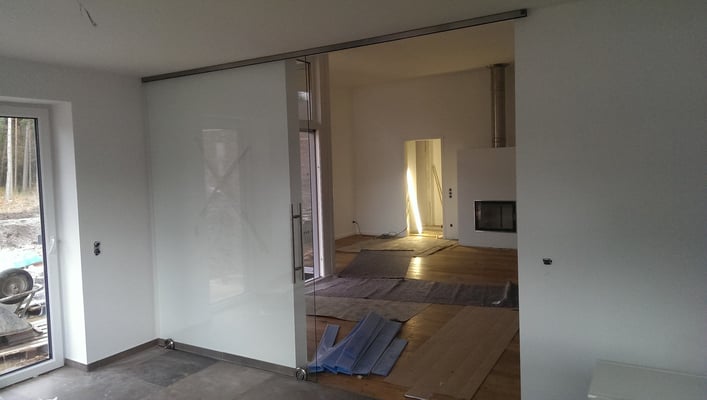 Einflüglige Schiebetür in ESG 10mm Deckenhoch mit Laufprofil in Edelstahloptik und einem Stoßgriff aus Edelstahl und einer Höhe von 80cm.