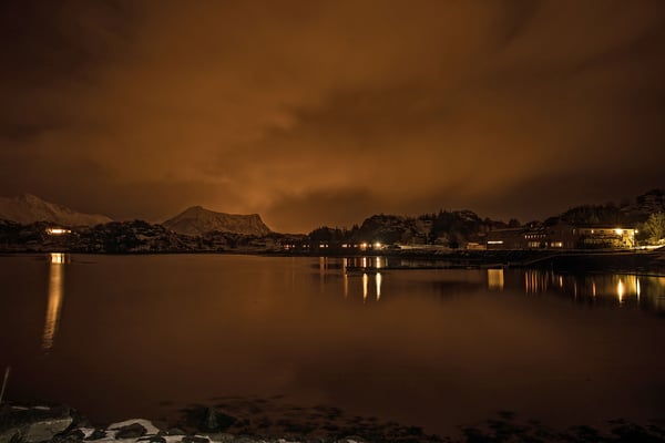 Nordlichter waren an unserem ersten Abend keine zu sehen, aber die weit verstreuten Lichtquellen zauberten trotzdem ihr Licht in den bewölkten Nachthimmel. Rechts im Bild unsere Unterkunft in Orsvagvaer