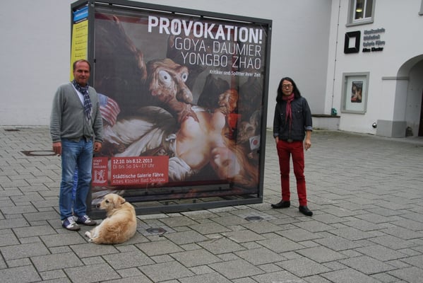 Yongbo Zhao with a friend and collector in front of the exhibition poster "Provocation! Goya, Daumier and Yongbo Zhao - Critics and Mockers of their Tmes" at the Municipal Gallery "Fähre" at the Old Cloister Bad Saulgau, 2013