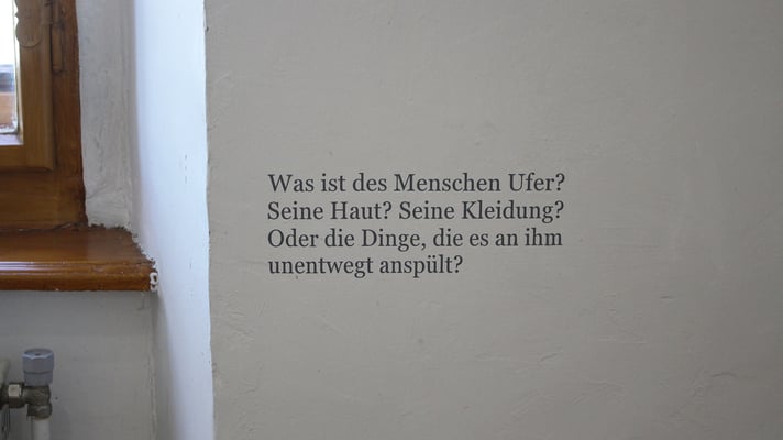 Ausstellung "Menschenufer" Großer Raum: Wandtext neben "Verpackung und Dinge - Eine Irritation"