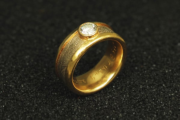 Gelbgoldring mit umlaufendem, in Weißgold gegossenem Handabdruck und rund gefaßtem Brillant